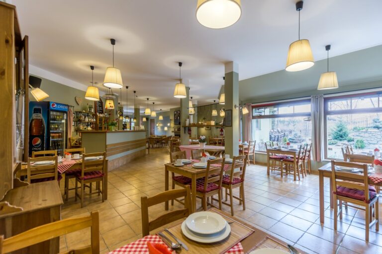 Sala restauracyjna z barem, stolikami i dużym oknem wychodzącym na ogród