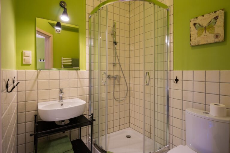 Łazienka z narożną kabiną prysznicową, umywalką i zielonymi ścianami