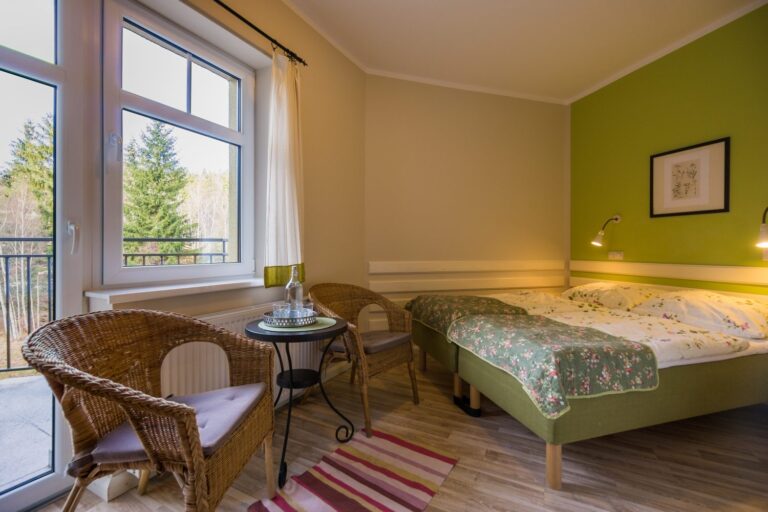 Pokój z dwoma łóżkami i wiklinowymi fotelami przy oknie balkonowym z widokiem na las