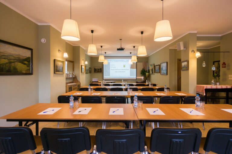 Sala konferencyjna w Domu pod Koziołkami przygotowana do szkolenia, z ekranem projekcyjnym i stołami