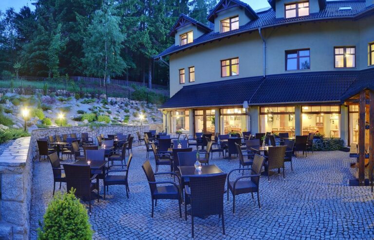Rozświetlony taras Domu pod Koziołkami o zmierzchu ze stolikami przy oświetlonej sali restauracyjnej